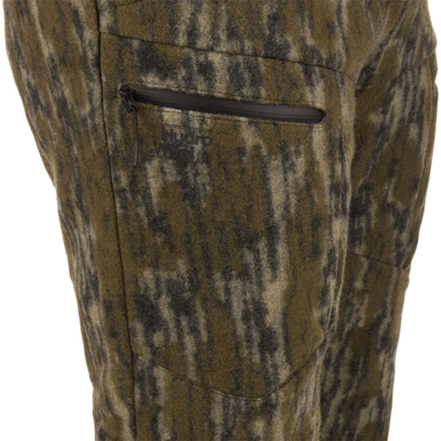 Midweight Hydrowool Softshell Pant with Scent Control close-up shows a camo wool-blend fabric with a waterproof zipper pocket and Hydro Wool logo, ideal for outdoor adventures.