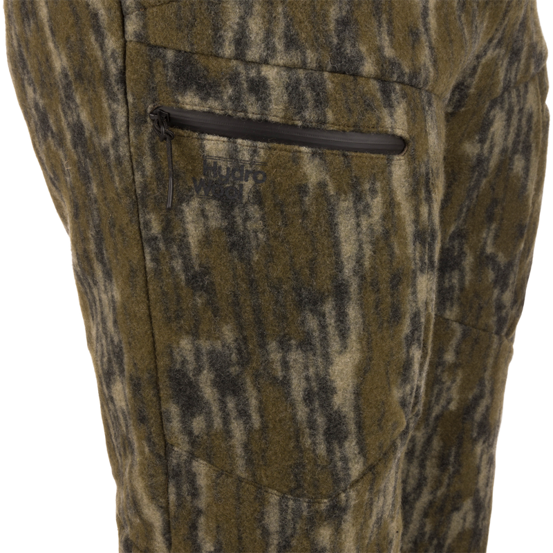 Midweight Hydrowool Softshell Pant with Scent Control close-up shows a camo wool-blend fabric with a waterproof zipper pocket and Hydro Wool logo, ideal for outdoor adventures.