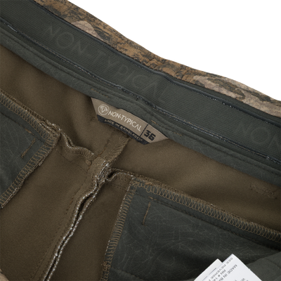 Close-up of the interior waistband of these olive green Nontypical Non-Typical Pursuit Softshell Pant with Agion Active X2 pants, featuring a camouflage-patterned trim, a size 36 label, and a brand tag.