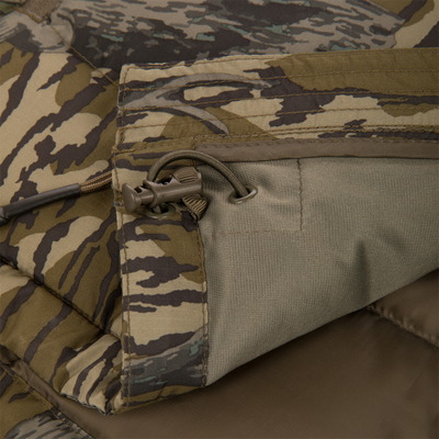 Close-up of the Non-Typical Down Jacket with Agion Active X2 by Nontypical in camouflage, featuring a zippered pocket with drawstring and toggle, plus detailed stitching in brown, olive, and tan fabric.