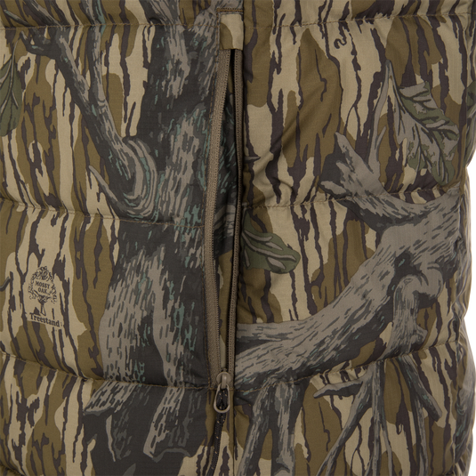 Close-up of the Non-Typical Down Vest with Agion Active X2 by Nontypical, featuring a camouflage pattern with tree branch designs in green, brown, and gray, and a partially unzipped vertical zipper.