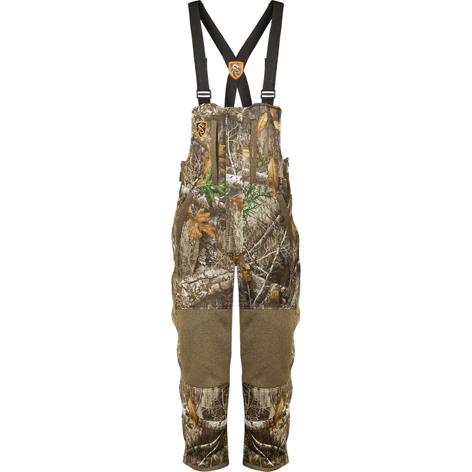 A youth silencer bib with Agion Active XL, featuring camouflage overalls with straps, vertical pockets for hunting gear, and a durable, warm, and breathable design.