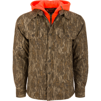 Men’s hunting-style jacket with Mossy Oak Bottomland camo, featuring blaze-orange hood, snap closure, and chest pockets, showcasing Drake Waterfowl's durable, functional hunting apparel.