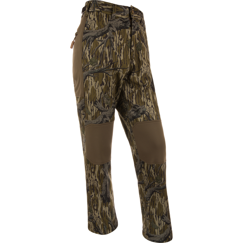 Youth Endurance Pant with woodland camo print, reinforced knees, zippered side pocket, and adjustable waist, designed for durability and flexibility in outdoor activities.