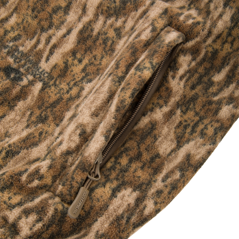 Close-up of the Non-Typical Windproof Layering Vest's fuzzy camouflage fleece fabric, highlighting a partially open zippered pocket, ideal for outdoor activities.