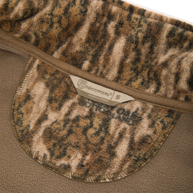 Close-up of Non-Typical Windproof Layering Vest's collar, showcasing camouflage fleece lining and tag, highlighting this windproof, water-resistant vest's durability for outdoor activities.