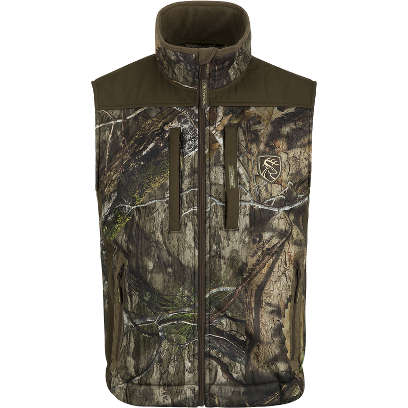 A Standstill Windproof Vest with Agion Active XL® featuring a camouflage pattern and logo of a deer. Perfect for mid-to-late season hunting, it offers soft, quiet, and durable fabric. Ideal for layering or wearing over a mid-layer.