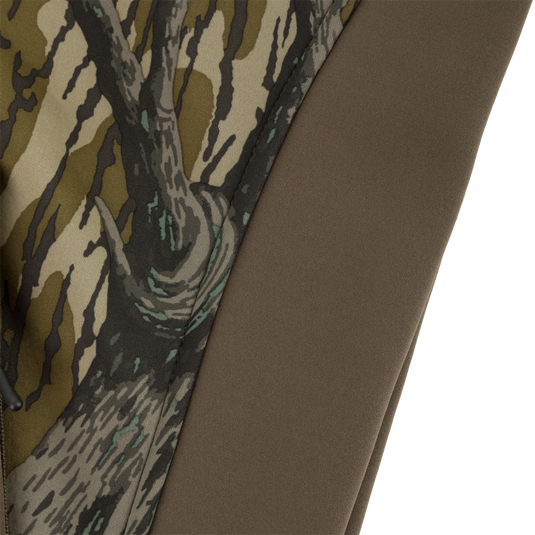 Close-up of a Youth Endurance Full Zip Jacket with Hood, featuring a tree bark camouflage pattern on one side and a solid brown, microfiber stretch fabric on the other.