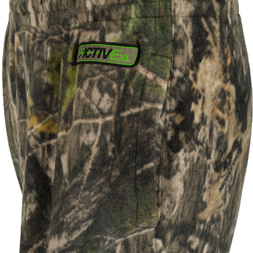 A pair of camouflage shorts with a close-up of a patch. These Storm Front Fleece Midweight 4-Way Stretch Pants are perfect for big game hunters, providing quiet, warm, and moisture-wicking insulation. Made with 200-gram 4-Way Stretch Fleece, they feature Agion Active XL® scent control technology, a tapered leg and cuff, two slash hand pockets, and an elastic waistband. Ideal for the hunting season.