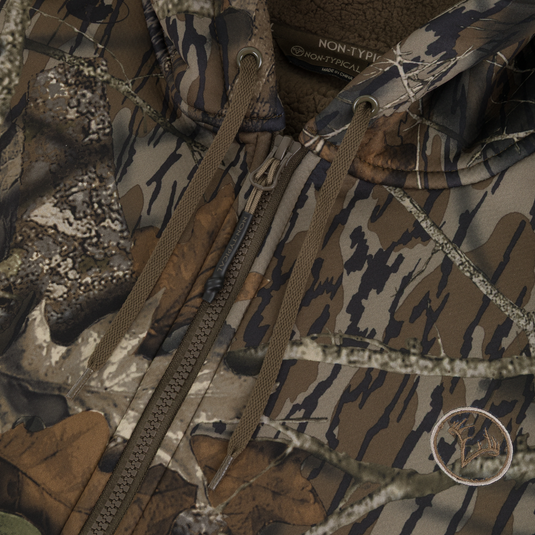 Close-up of the Non-Typical Slacker Quarter Zip Hoodie by Nontypical, featuring a camo pattern, brown drawstrings, deer antler patch, and thick fleece lining—perfect for hunting or outdoor use.