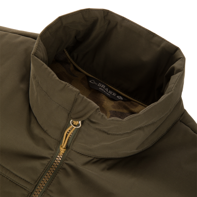 Close-up of the Delta Featherless Down Vest showing its stand-up collar, brass zipper with paracord pull, and camouflage-print lining with “Drake’s • Made in China” label.