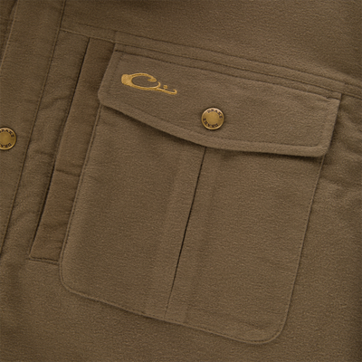Close-up of Delta Moleskin Shirt Jacket's flap pocket with brass snap-button stamped “DRAKE” and gold-thread embroidered emblem, showcasing durable cotton moleskin material.