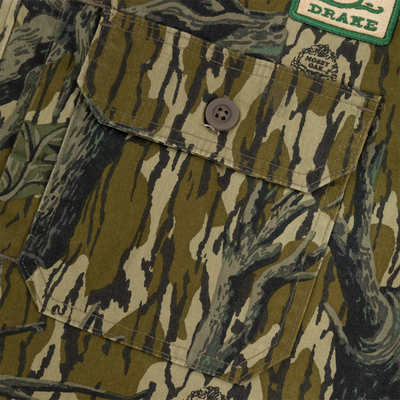 Close-up of a camouflage-patterned pocket with a brown button on the Campfire Canvas Bomber Jacket by Lifestyle; pocket flap down and a green and white DRAKE patch visible at the top right.