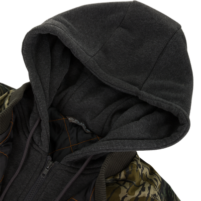 A close-up of the Lifestyle Campfire Canvas Bomber Jacket features a dark gray hood, camouflage-patterned shoulders, black lining, a zipper, and visible orange stitching.