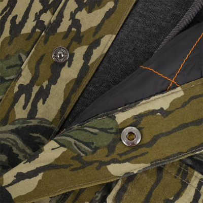 Close-up of the Campfire Canvas Bomber Jacket by Lifestyle, featuring a snap button, green-brown camo pattern, black lining with orange stitching, and dark gray fabric underneath.