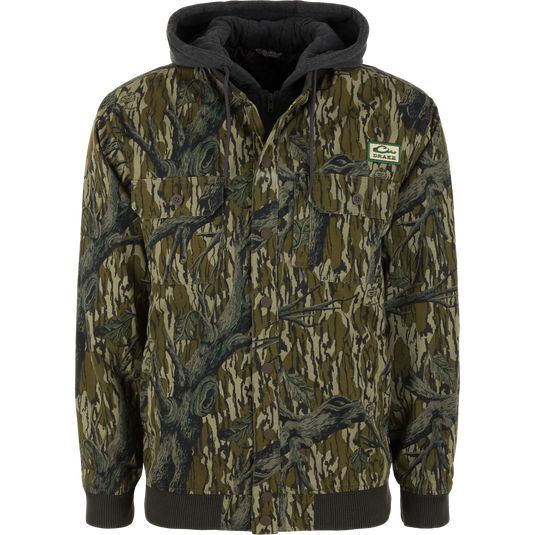 The Lifestyle Campfire Canvas Bomber Jacket in Mossy Oak Original Treestand features two chest pockets, a front zipper, and a green logo patch on the left chest.