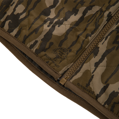 Close-up of a Lifestyle Delta Quilted Vest in a green and brown camouflage print, featuring a front zipper and a Mossy Oak Bottomland logo.
