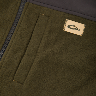 Close-up of the Camp Fleece Vest featuring olive-green fleece, quilt-style stitching, a plastic zipper, and a beige label, highlighting its durable, water-resistant design.