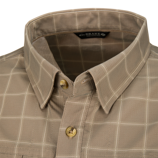 Close-up of a tan Wingshooter Hunter Creek Shirt featuring moisture-wicking fabric, a subtle white grid pattern, and a buttoned collar.