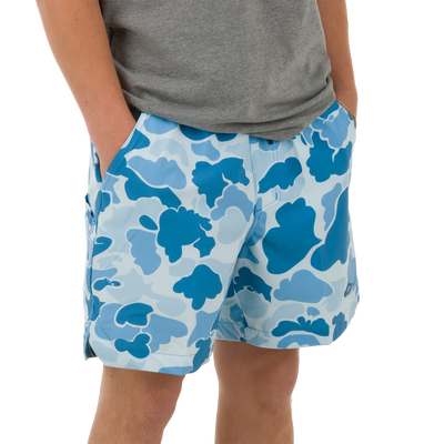 Person wearing Lake Shore Dock Short with floral camo pattern, plain grey T-shirt, and gold chain bracelet. Shorts feature elastic waistband and mesh-lined pockets.