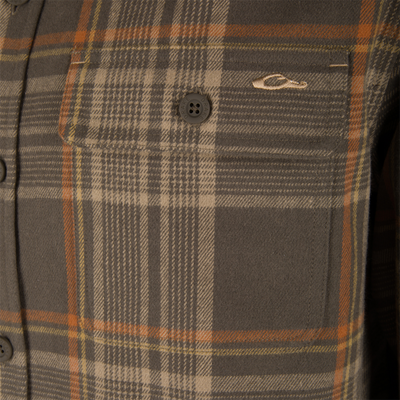 Legacy Flannel Plaid Shirt pocket close-up, showing a brown plaid pattern with a DRAKE button and embroidered fish or duck logo above the flap.