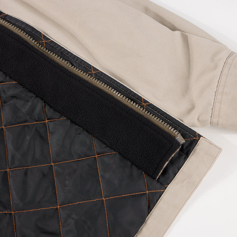 Close-up of the Campfire Canvas Shirt Jac Hoodie's hem, showcasing beige fabric, metal zipper, black quilt-stitched lining, and a fleece strip along the seam.