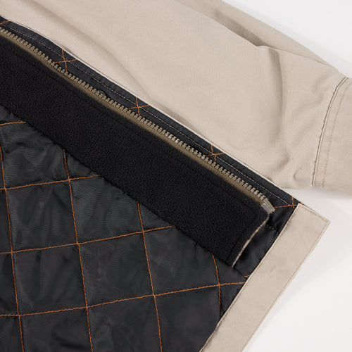 Close-up of the Campfire Canvas Shirt Jac Hoodie's hem, showcasing beige fabric, metal zipper, black quilt-stitched lining, and a fleece strip along the seam.