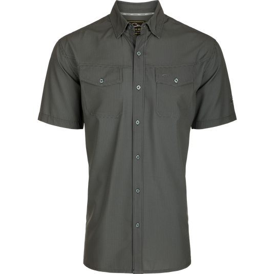 A close-up of the Traveler's Check Shirt S/S, a lightweight, breathable poly/spandex shirt with a hidden button-down collar and split tail hem. Ideal for the man on the go, it offers Four Way Stretch, sun protection, moisture-wicking, and quick-drying features.