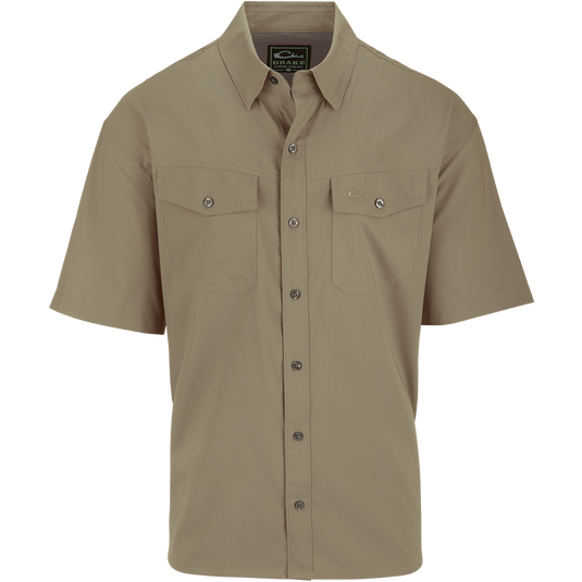 A close-up of the Traveler's Solid Dobby Shirt S/S, a short-sleeved shirt with hidden button-down collar and two chest pockets with button-through flaps. Made of 100% Polyester textured dobby fabric, it features UPF30 sun protection and moisture-wicking properties. Versatile for any season.