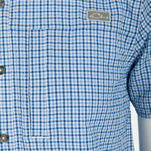 A close-up of the Classic Seersucker Grid Check Shirt S/S, featuring a blue and white checkered pattern, hidden button-down collar, and zippered chest pocket.