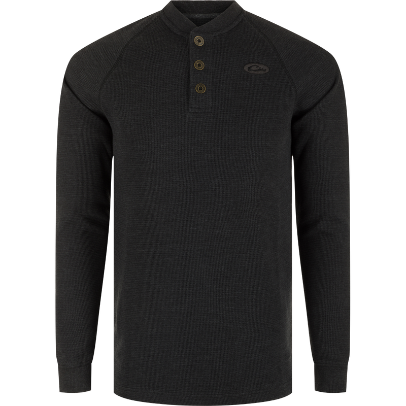 A black long sleeve Henley shirt with metal logo buttons, raglan sleeves, rib knit collar, and cuffs. Made of waffle mélange fabric for comfort, antimicrobial, and moisture-wicking properties. Split tail hem for versatile styling.