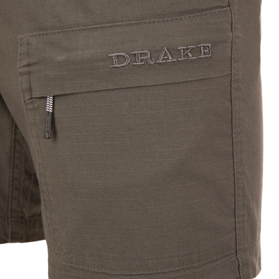 Close-up of the Drake 9-Pocket Ripstop Short, featuring a flap pocket with DRAKE embroidery and a zip-pull tab, designed for outdoor adventures.