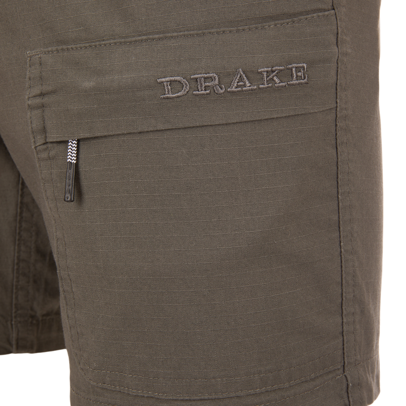 Close-up of the Drake 9-Pocket Ripstop Short, featuring a flap pocket with DRAKE embroidery and a zip-pull tab, designed for outdoor adventures.