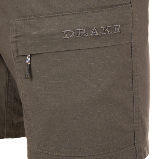 Close-up of the Drake 9-Pocket Ripstop Short, featuring a flap pocket with DRAKE embroidery and a zip-pull tab, designed for outdoor adventures.