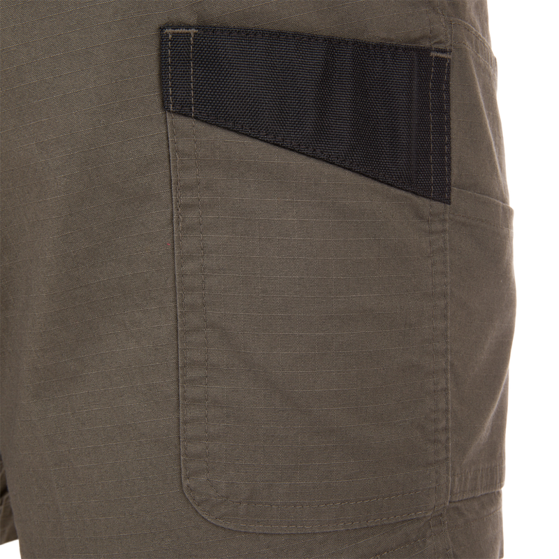 Close-up of 9 Pocket Ripstop Short's olive-green ripstop pocket with black reinforced trim, showcasing durable utility-style design for outdoor adventures.