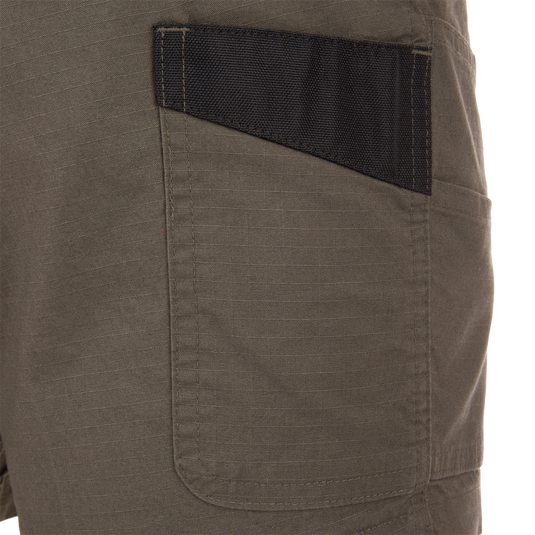 Close-up of 9 Pocket Ripstop Short's olive-green ripstop pocket with black reinforced trim, showcasing durable utility-style design for outdoor adventures.