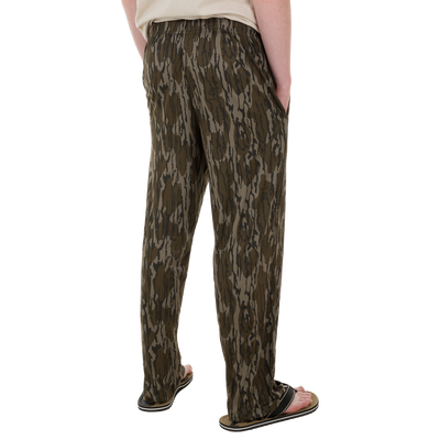 Person wearing Drake Lounge Pant in camouflage pattern with elastic waistband and side pockets, paired with black flip-flops, showcasing relaxed, post-hunting comfort.