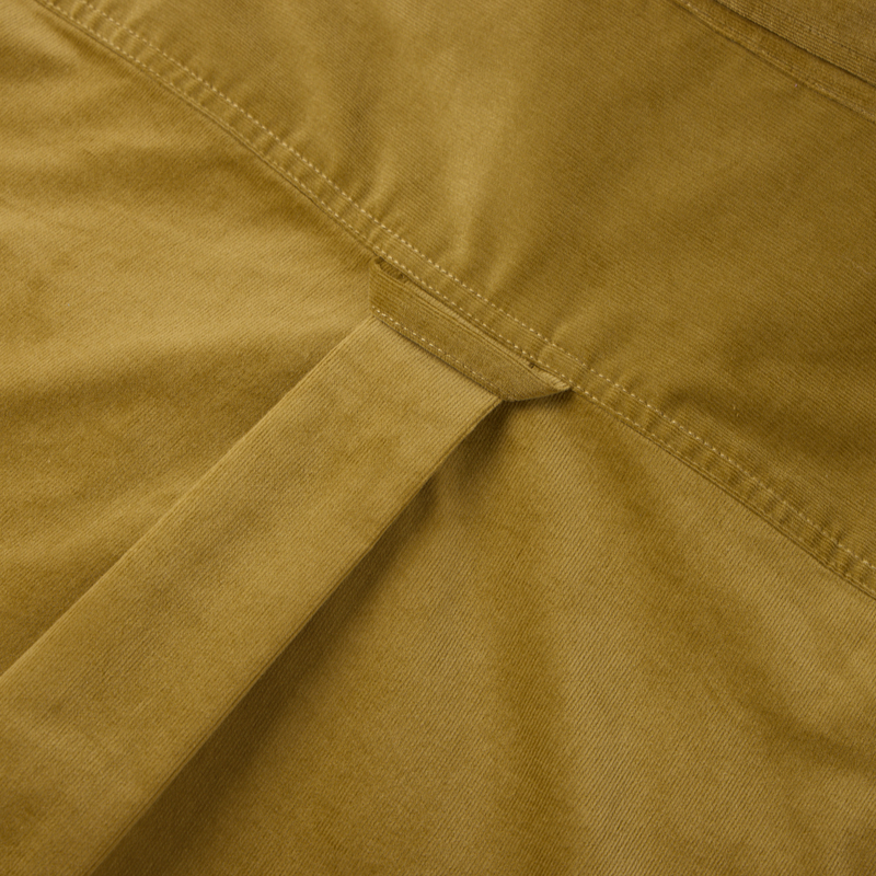 Close-up of a mustard-colored garment with a cinch strap, showcasing Drake's Midwale Corduroy Shirt featuring stretch fabric, button-down collar, and sculpted hem.