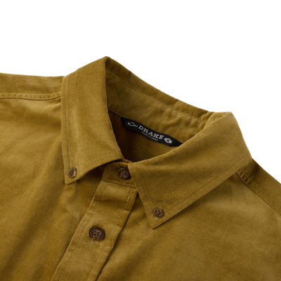 Close-up of the Midwale Corduroy Shirt collar and buttons, showcasing the mustard-yellow corduroy fabric with stretch for comfort, labeled DRAKE, size S.
