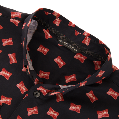 Close-up of the Cotton Drake Life Print Short Sleeve Shirt, featuring a black button-up with red Drake logo motif and two flap pockets.