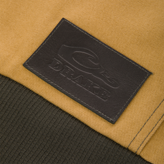 Close-up of a tan Duck Canvas Work Jacket featuring a brown rectangular patch embossed with a logo and the word DRAKE.