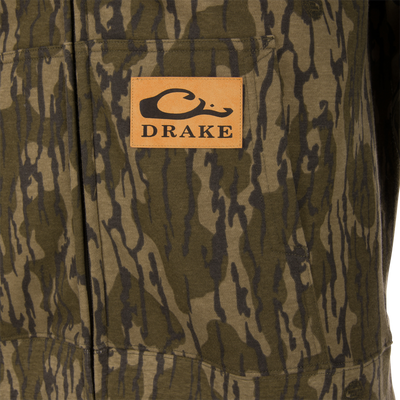 Close-up of Three End Full Zip Work Hoodie with camo pattern, kangaroo pocket, and tan leather patch featuring Drake's stylized “D”/fish-hook logo.