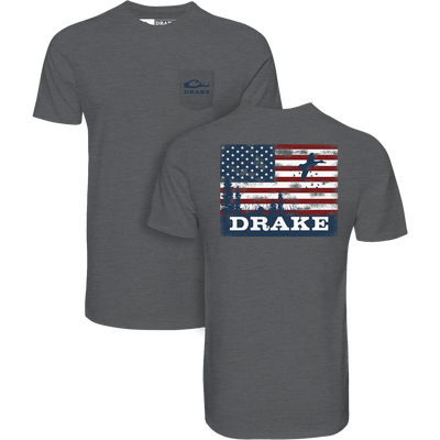 Americana Scenic Flag T-Shirt featuring a front Drake logo pocket and back distressed American flag with flying ducks, symbolizing the Drake Waterfowl brand's outdoor spirit.
