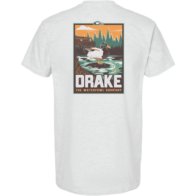 Mallard Blind Scene T-Shirt featuring a drake in a marsh with duck blind silhouette, evergreens, and orange sky. Bold DRAKE text highlights the Waterfowl Company's theme.