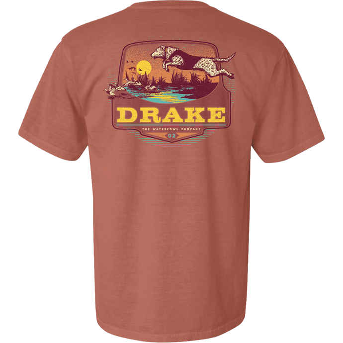 Don’t Let Em Behind You T-Shirt featuring a hunting dog graphic leaping over a marsh with ducks, sunset backdrop, and Drake logo on the back.