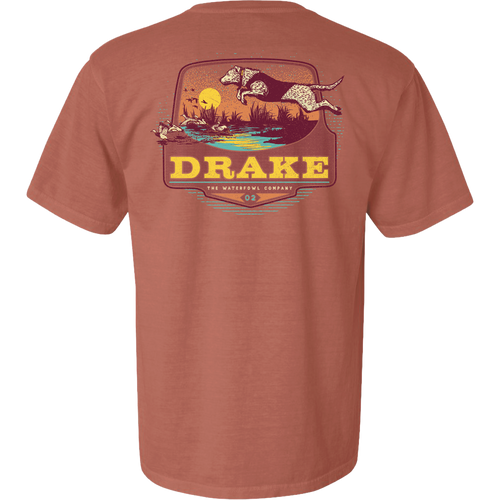 Don’t Let Em Behind You T-Shirt featuring a hunting dog graphic leaping over a marsh with ducks, sunset backdrop, and Drake logo on the back.