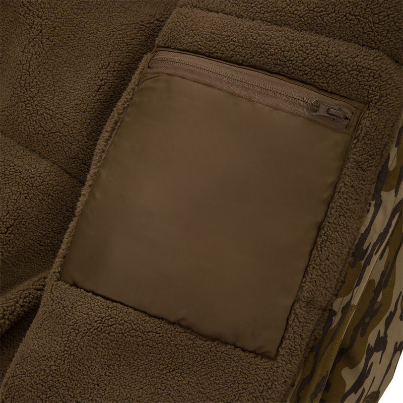 Close-up of the Throwback 80 Insulated Sport Bomber Jacket, showcasing its brown sherpa fleece lining, nylon pocket with zipper, and camouflage fabric hinting at a hunting-themed design.