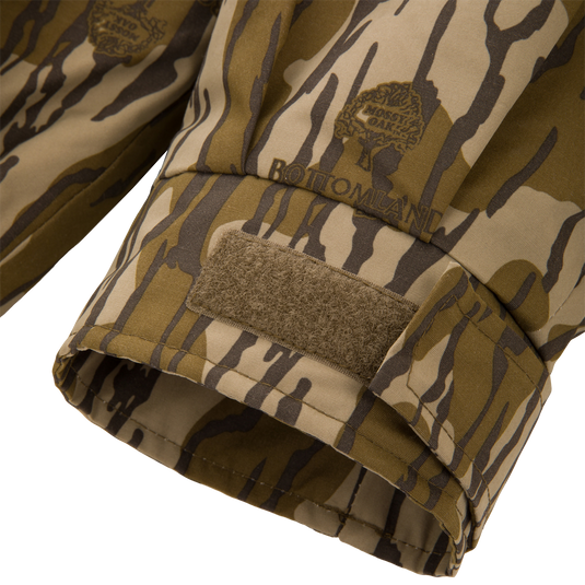 Throwback 80 Insulated Sport Bomber Jacket cuff in Bottomland camo, featuring Velcro strap and branded logo, showcasing durable design for hunting.