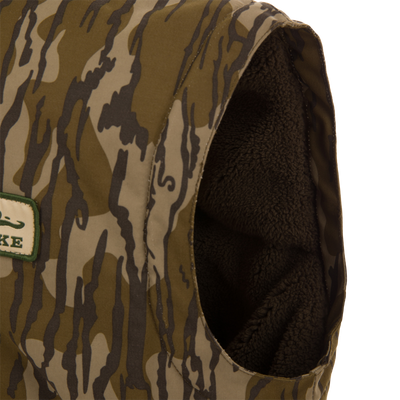 Throwback 80 Sport Vest, a sleeveless camo vest with fleece lining, features large pockets, brass zipper, and wind flap, ideal for outdoor adventures.