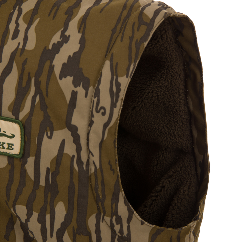 Throwback 80 Sport Vest, a sleeveless camo vest with fleece lining, features large pockets, brass zipper, and wind flap, ideal for outdoor adventures.